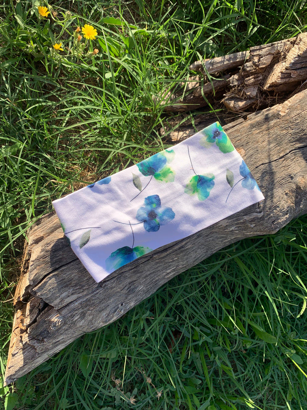 Bandeau cheveux L'Original imprimé floral bleu et vert sur fond blanc, posé à plat sur une souche en bois dans l'herbe, coton bio GOTS fait main, MALOU au Fil des Saisons