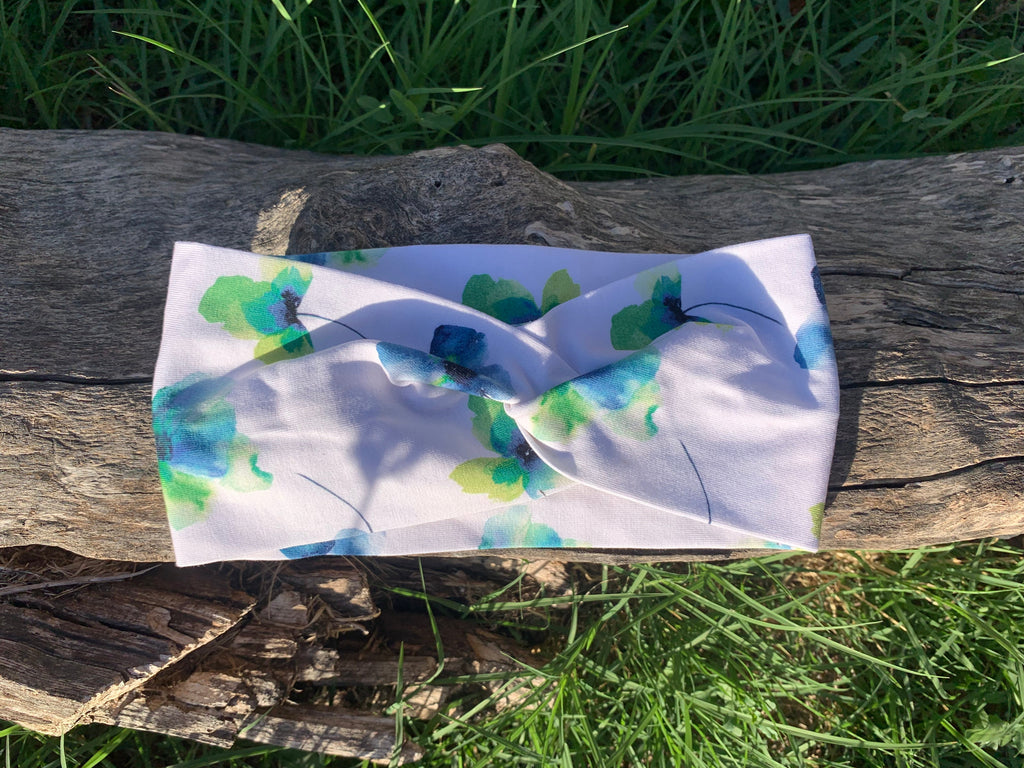 Bandeau cheveux L'Original imprimé floral bleu et vert sur fond blanc, posé à plat sur une souche en bois dans l'herbe, coton bio GOTS fait main, MALOU au Fil des Saisons