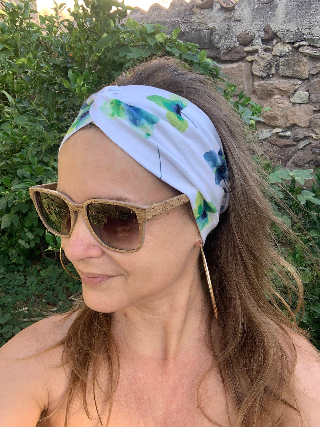 Bandeau cheveux L'Original imprimé floral bleu et vert sur fond blanc, posé à plat sur une souche en bois dans l'herbe, coton bio GOTS fait main, MALOU au Fil des Saisons