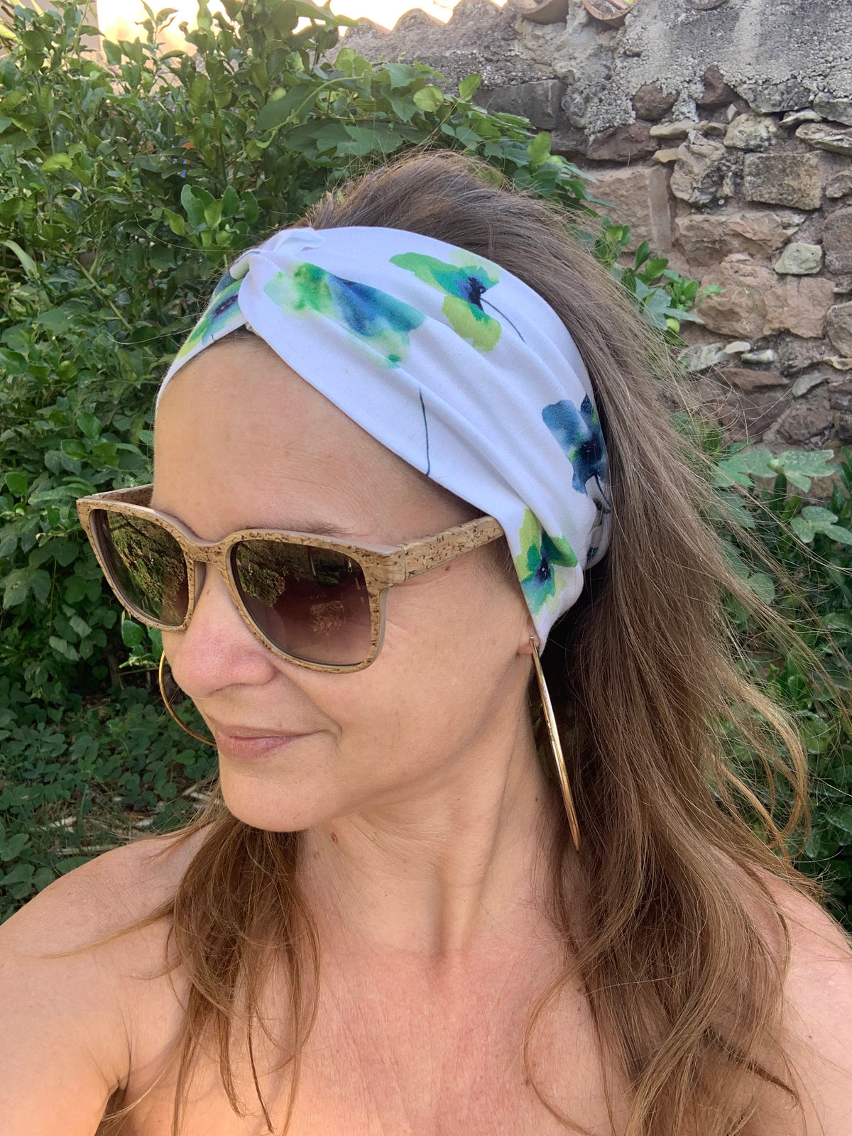 Bandeau cheveux L'Original imprimé floral bleu et vert sur fond blanc, posé à plat sur une souche en bois dans l'herbe, coton bio GOTS fait main, MALOU au Fil des Saisons