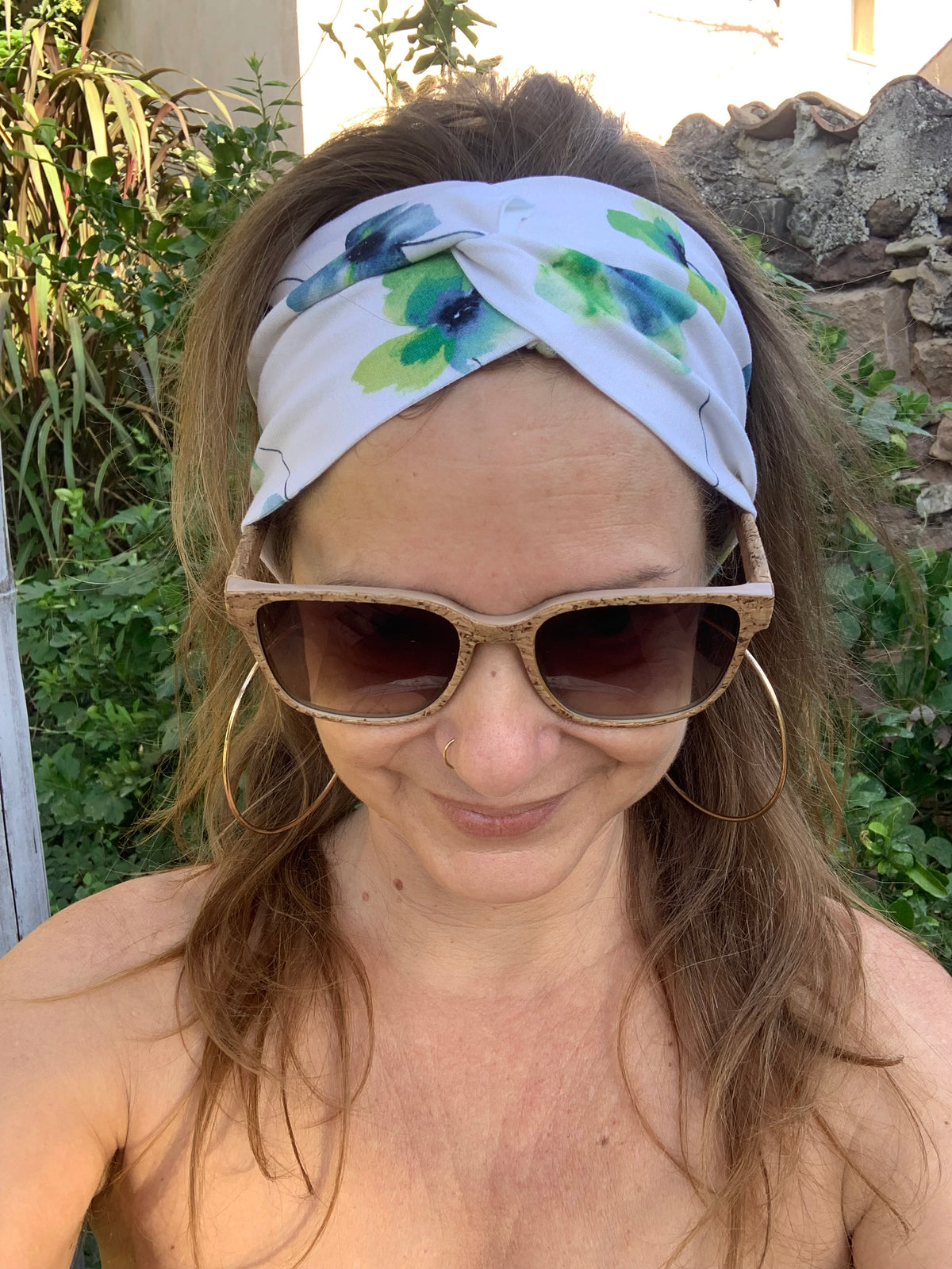 Bandeau cheveux L'Original imprimé floral bleu et vert sur fond blanc, posé à plat sur une souche en bois dans l'herbe, coton bio GOTS fait main, MALOU au Fil des Saisons