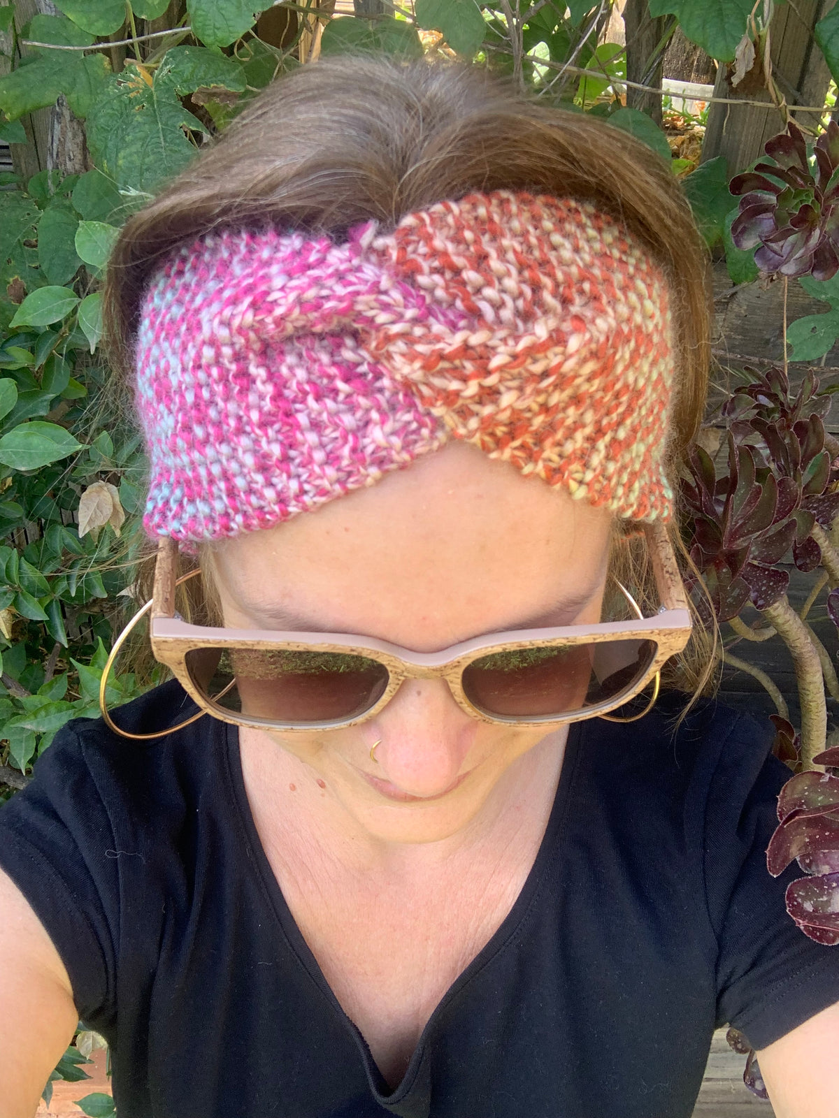 Femme portant un bandeau tricoté main au point mousse tons chauds rose et orange avec nœud twist, accessoire hivernal artisanal MALOU au Fil des Saisons