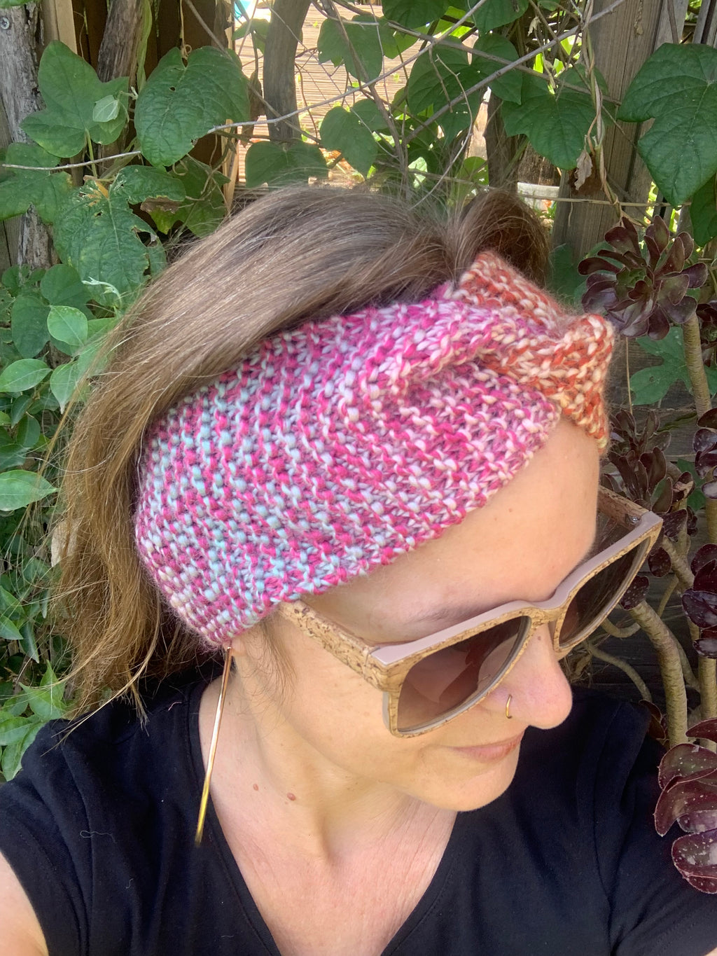 Femme portant un bandeau tricoté main au point mousse tons chauds rose et orange avec nœud twist, accessoire hivernal artisanal MALOU au Fil des Saisons