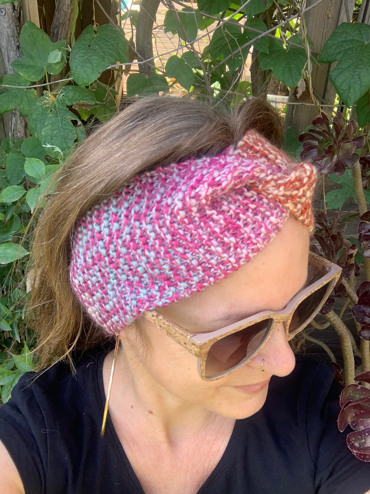 Femme portant un bandeau tricoté main au point mousse tons chauds rose et orange avec nœud twist, accessoire hivernal artisanal MALOU au Fil des Saisons