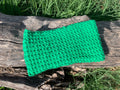 Bandeau cheveux tricoté à la main au point de riz vert prairie vif 100% acrylique, posé à plat sur une souche en bois dans l'herbe, fabrication artisanale en France, MALOU au Fil des Saisons