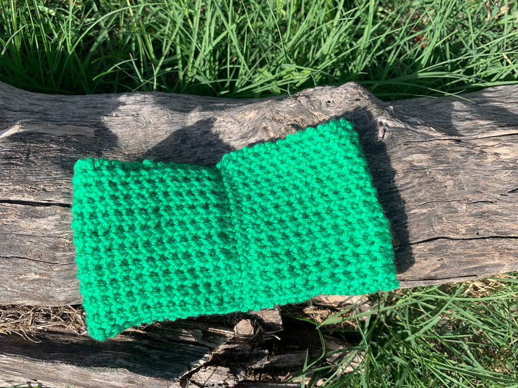 Bandeau cheveux tricoté à la main au point de riz vert prairie vif 100% acrylique, posé à plat sur une souche en bois dans l'herbe, fabrication artisanale en France, MALOU au Fil des Saisons