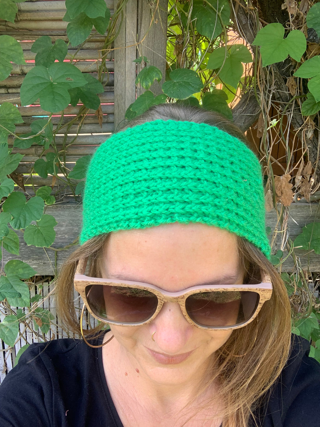 Bandeau cheveux tricoté à la main au point de riz vert prairie vif 100% acrylique, posé à plat sur une souche en bois dans l'herbe, fabrication artisanale en France, MALOU au Fil des Saisons