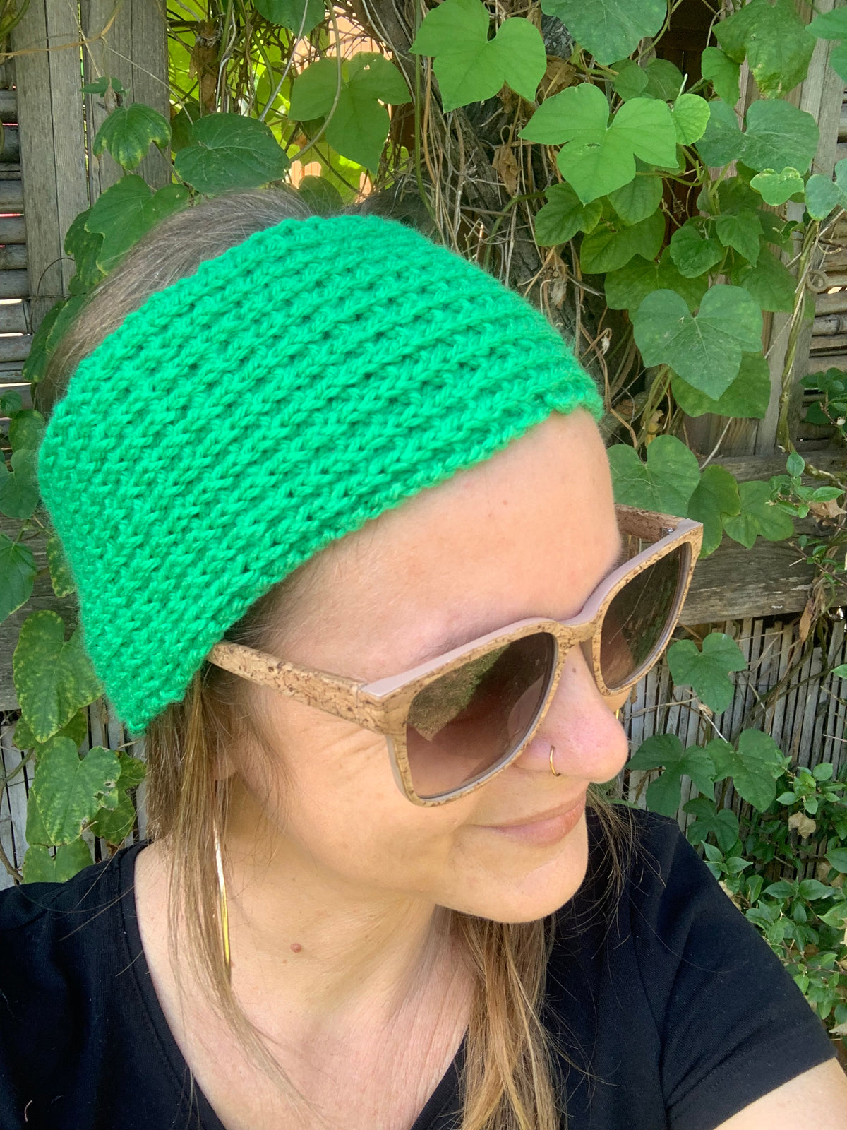 Bandeau cheveux tricoté à la main au point de riz vert prairie vif 100% acrylique, posé à plat sur une souche en bois dans l'herbe, fabrication artisanale en France, MALOU au Fil des Saisons