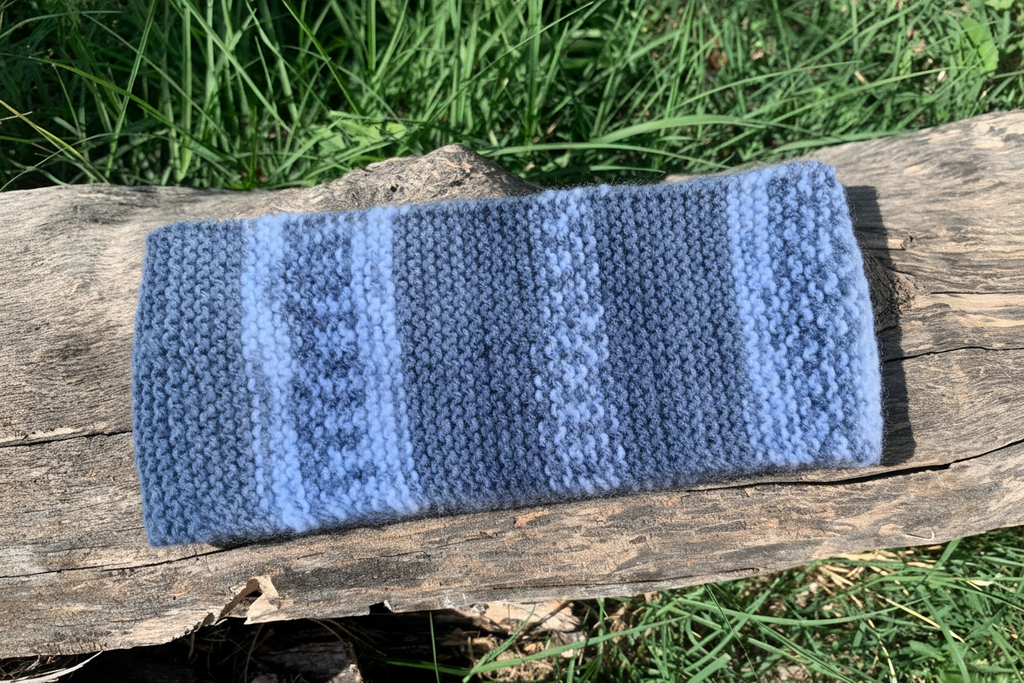 Bandeau tricoté gris et blanc posé sur un tronc d’arbre allongé, accessoire cheveux artisanal